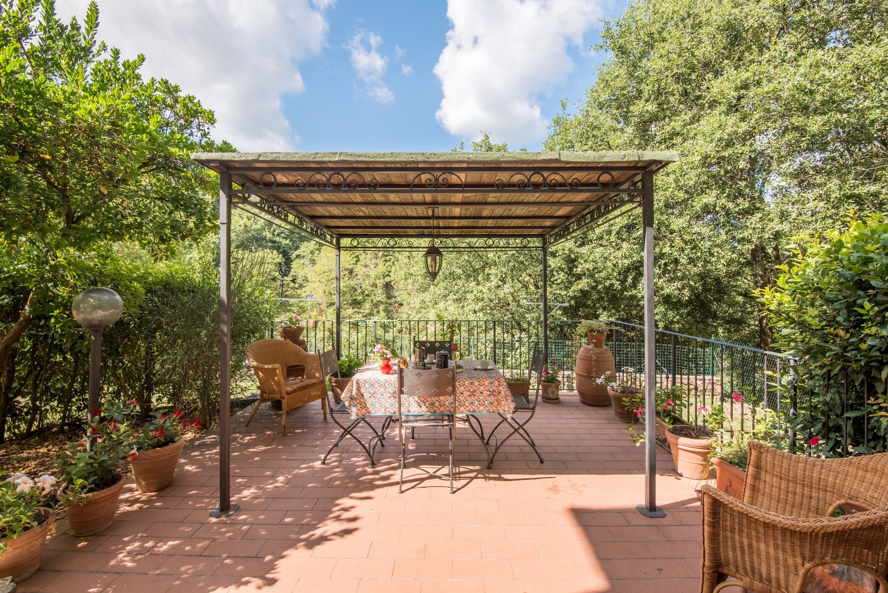 A covered patio area with a table and chairs, surrounded by potted plants and a pergola.
