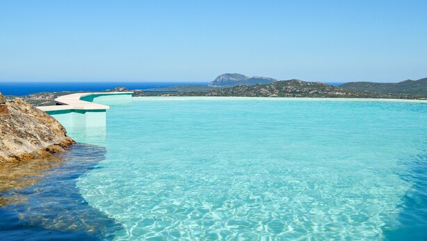 A clear blue pool with a curved edge, surrounded by rocky terrain and a distant mountain. - Holiday Home "Villa Maryna" with Sea View, Private Terrace, Pool and Wi-Fi (Olbia)
