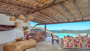 An outdoor dining area with a view of the sea, wooden furniture, and hanging baskets. - Holiday Home "Villa Maryna" with Sea View, Private Terrace, Pool and Wi-Fi (Olbia)