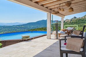 Un espacio al aire libre techado con piscina, mobiliario de mimbre y vistas a un paisaje montañoso.