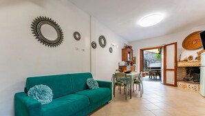 En stue med en teal-farvet sofa, et spiseområde med et bord og stole, og et køkken med en murstensvæg og et fjernsyn.