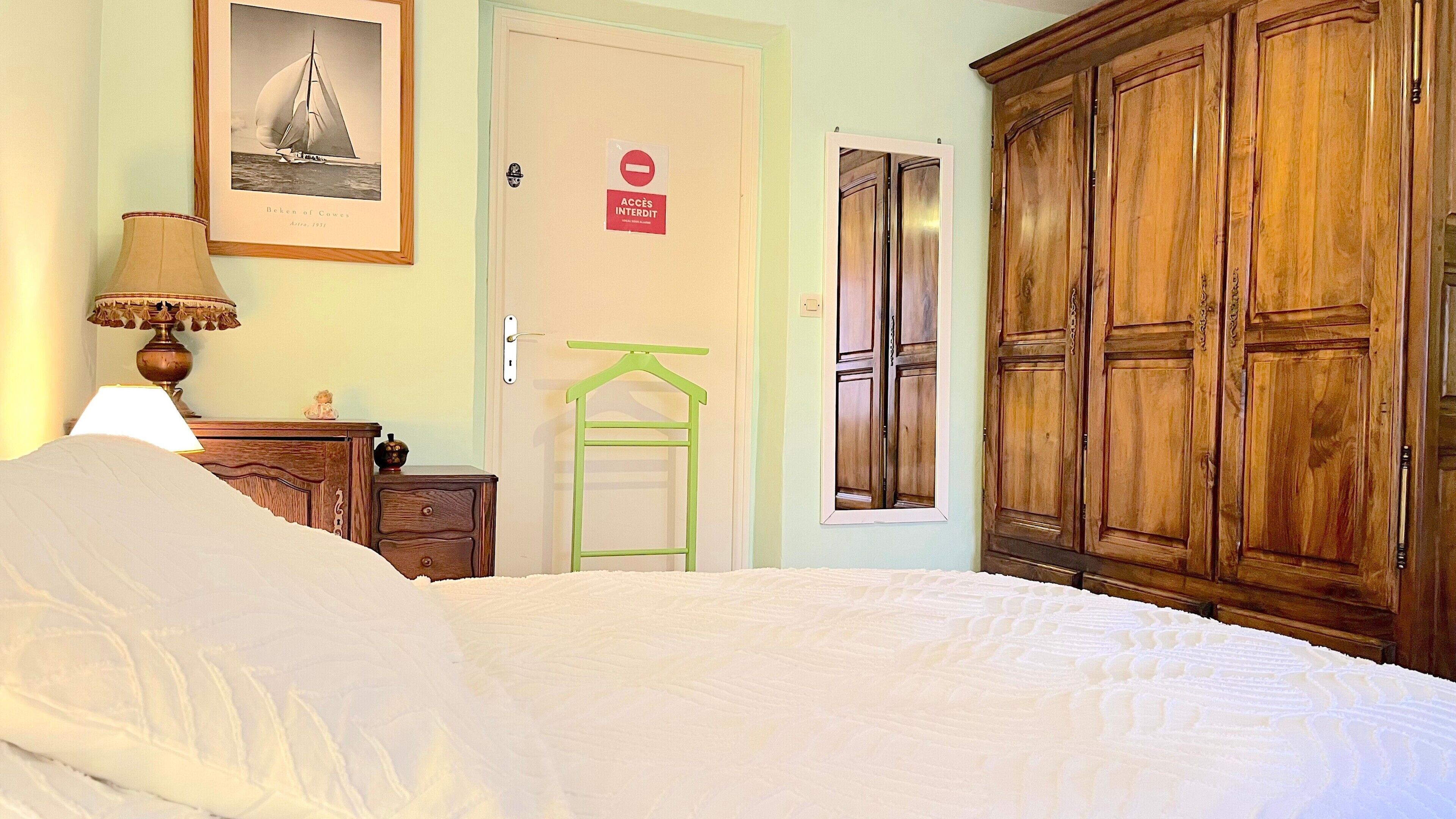 A bedroom with a bed, a dresser, a lamp, a framed picture, a door with a sign, and a wardrobe.