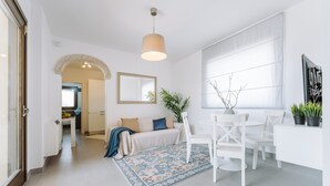 A modern interior with a dining area, a sofa, a patterned rug, and a large window. - Villa 'Delle Viole' with Private Pool, Wi-Fi and Air Conditioning (Quartu Sant'elena)