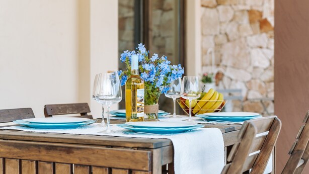 A wooden table set with blue plates, wine glasses, a bottle of wine, and a vase with blue flowers. - Villa 'Delle Viole' with Private Pool, Wi-Fi and Air Conditioning (Quartu Sant'elena)