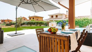 An outdoor patio with a table set for dining, a large umbrella, and a view of the surrounding neighborhood. - Villa 'Delle Viole' with Private Pool, Wi-Fi and Air Conditioning (Quartu Sant'elena)