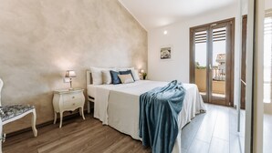 A bedroom with a bed, bedside tables, a bench, a balcony with a view, and a door. - Villa 'Delle Viole' with Private Pool, Wi-Fi and Air Conditioning (Quartu Sant'elena)