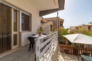 Een balkon met een tafel en stoelen, een witte parasol en een houten omheining.