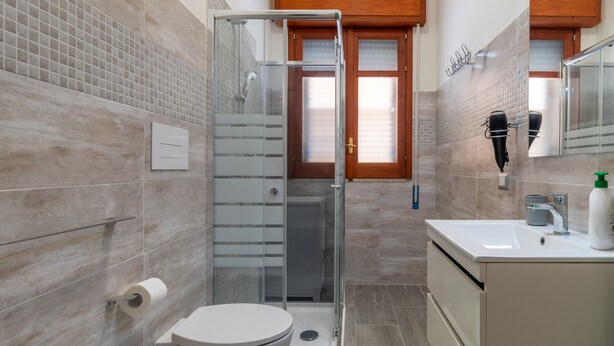 Un bagno con doccia vetro, un water, un lavandino con specchio e un armadietto in legno.