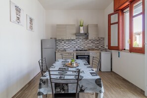 Een kleine keuken met een eettafel, stoelen, een koelkast, een fornuis en een raam met uitzicht.