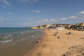 Uma praia com pessoas, guarda-sóis e edifícios ao fundo.