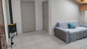 A room with a tiled floor, a grey sofa with a blue cover, a black heater, and a wooden ceiling. - Apartment near Verona with Mountain Views (Rovere' Veronese)
