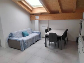 A small room with a wooden ceiling, a sofa with a cushion, a table with chairs, and a radiator.