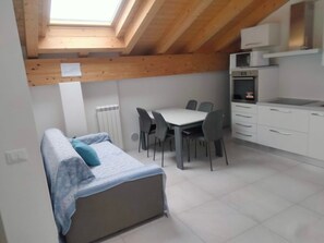 A compact room with a bed, a dining table with chairs, a kitchenette, and a skylight.