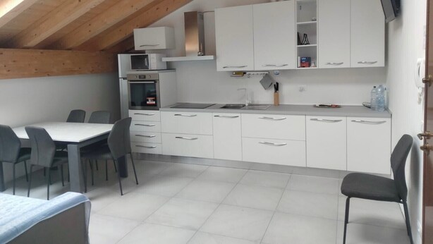 A compact kitchen with white cabinets, a microwave, and a stove. There is a dining area with a table and chairs. - Apartment near Verona with Mountain Views (Rovere' Veronese)