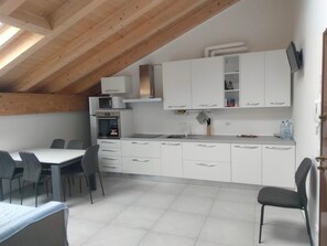 A compact kitchen with white cabinets, a microwave, and a stove. There is a dining area with a table and chairs.