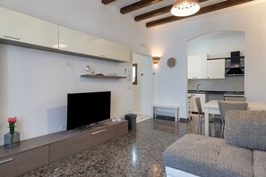A modern living room with a flat-screen TV, a sofa, a coffee table, and a kitchen in the background. - Holiday Home "Rosa Dei Venti" - Grottaglie (Grottaglie)