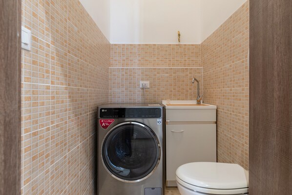 A compact bathroom with a washing machine, toilet, and sink. - Holiday Home "Rosa Dei Venti" - Grottaglie (Grottaglie)