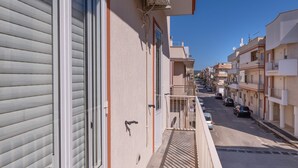 Ein Wohngebäude mit Balkon, Straßenansicht und geparkten Autos.