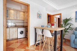A kitchen with wooden cabinets, a washing machine, a dining table with chairs, and a blue sofa in a living area.