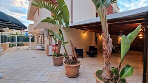 Une cour agrémentée de plantes en pot, une porte blanche et un bâtiment dont le sol est recouvert de carreaux.