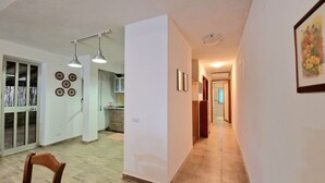 A hallway with a wooden floor, a dining area with a chair, and a kitchen with cabinets and a window. - Apartment 'Casa Alamar' with Private Garden, Wi-Fi and Air Conditioning (Alcamo)