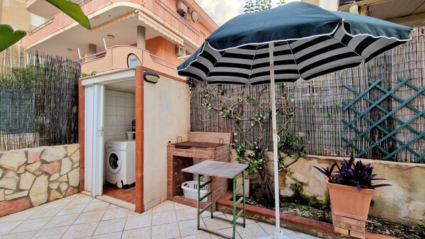 Une terrasse équipée d’un lave-linge, d’un barbecue et d’un parasol à rayures.
