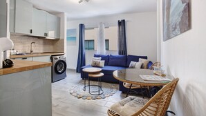Un espace de vie compact comprenant un coin cuisine, un canapé, une table à manger et un lave-linge.
