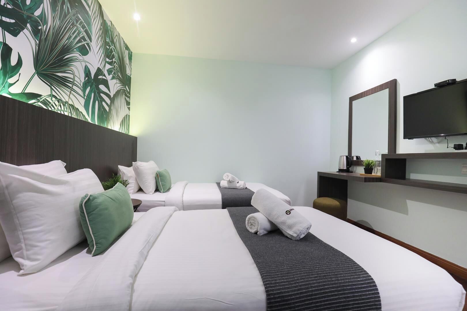 Habitación de hotel con dos camas, un espejo grande, un televisor de pantalla plana y una pared con diseño de hojas tropicales.