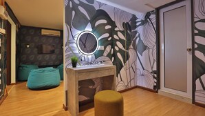 A room with a wooden floor, a round mirror on a console table, a green plant, and a wall with a leaf pattern. - Trevor Hotel by I Housing (Malacca City)