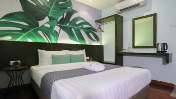 Una habitación de hotel con una cama, una mesita de noche, una pequeña mesa con una planta, un espejo grande y un equipo de aire acondicionado.