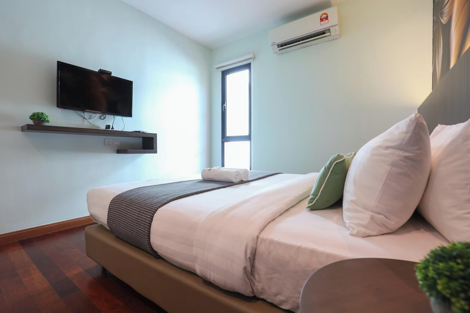 A modern bedroom with a bed, a mounted TV, an air conditioning unit, and a window.