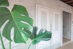 Una habitación con una planta verde grande, contraventanas blancas y un vidrio que da a otro espacio.