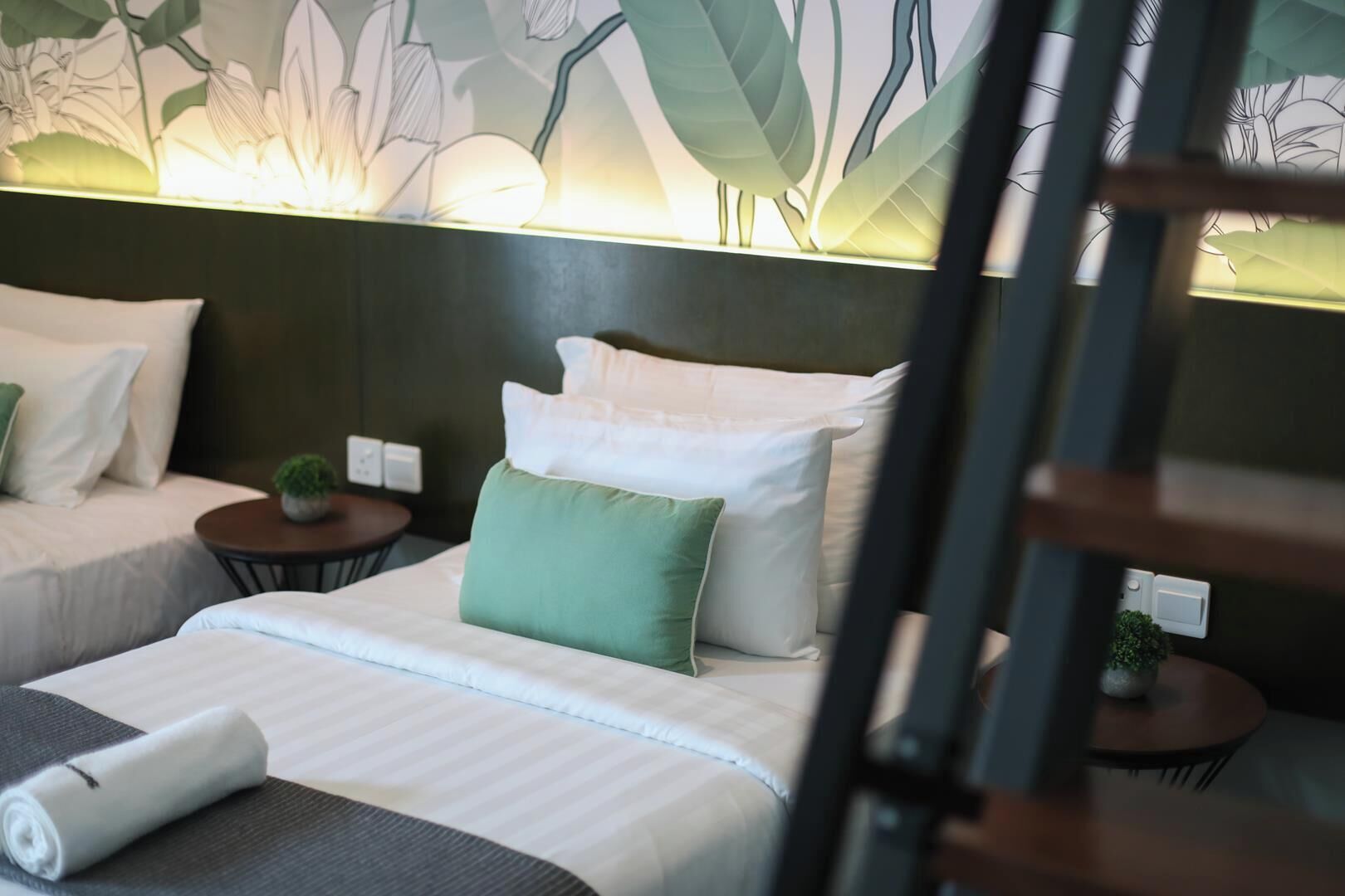 Quarto de hotel com duas camas, uma mesinha de cabeceira, um abajur e uma parede com padrão floral.