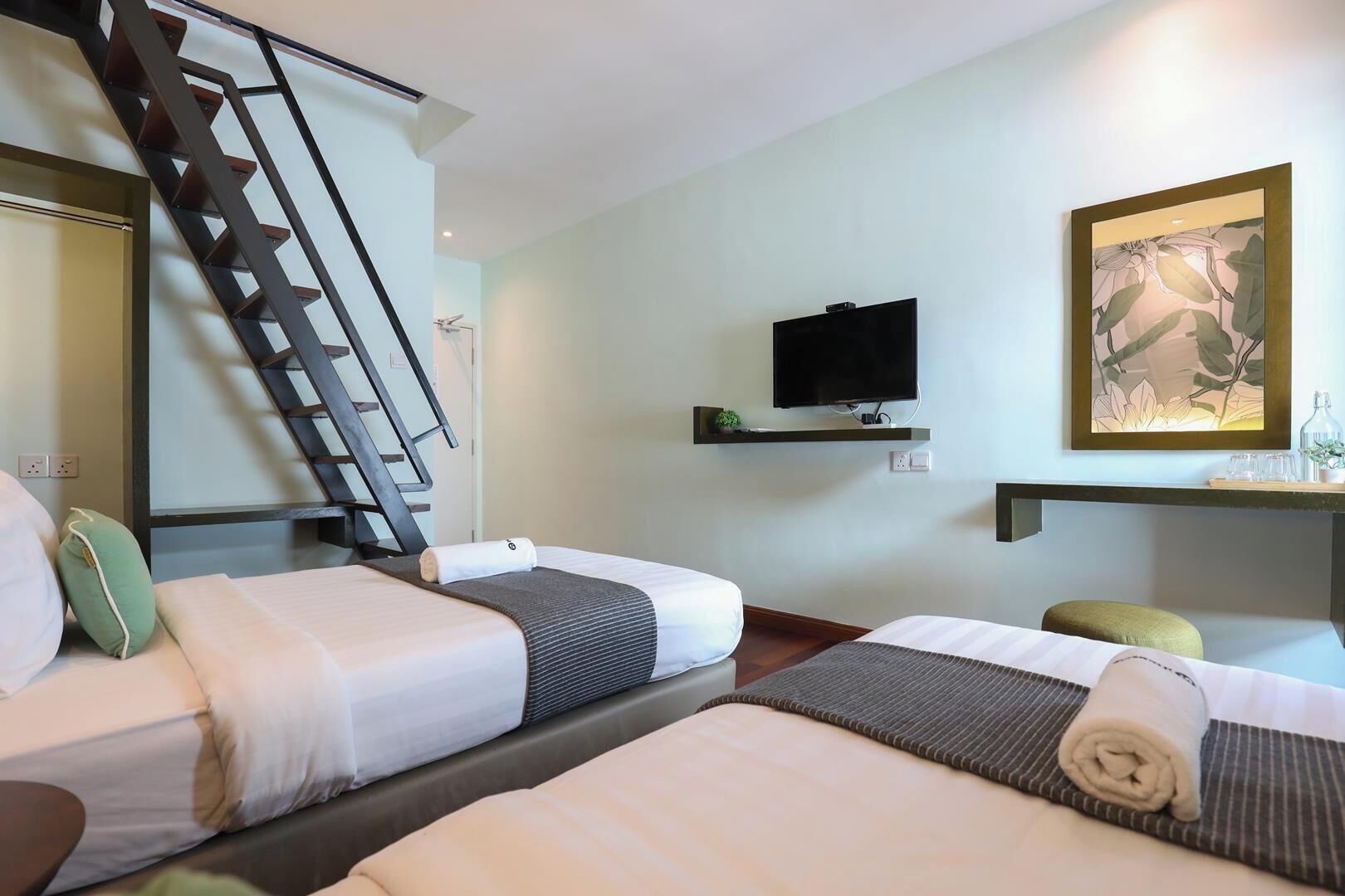A hotel room with two beds, a TV, a painting, and a desk with a plant.
