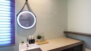 Un baño con un lavabo blanco, un espejo con luz, una planta pequeña en maceta y artículos de aseo en la encimera.