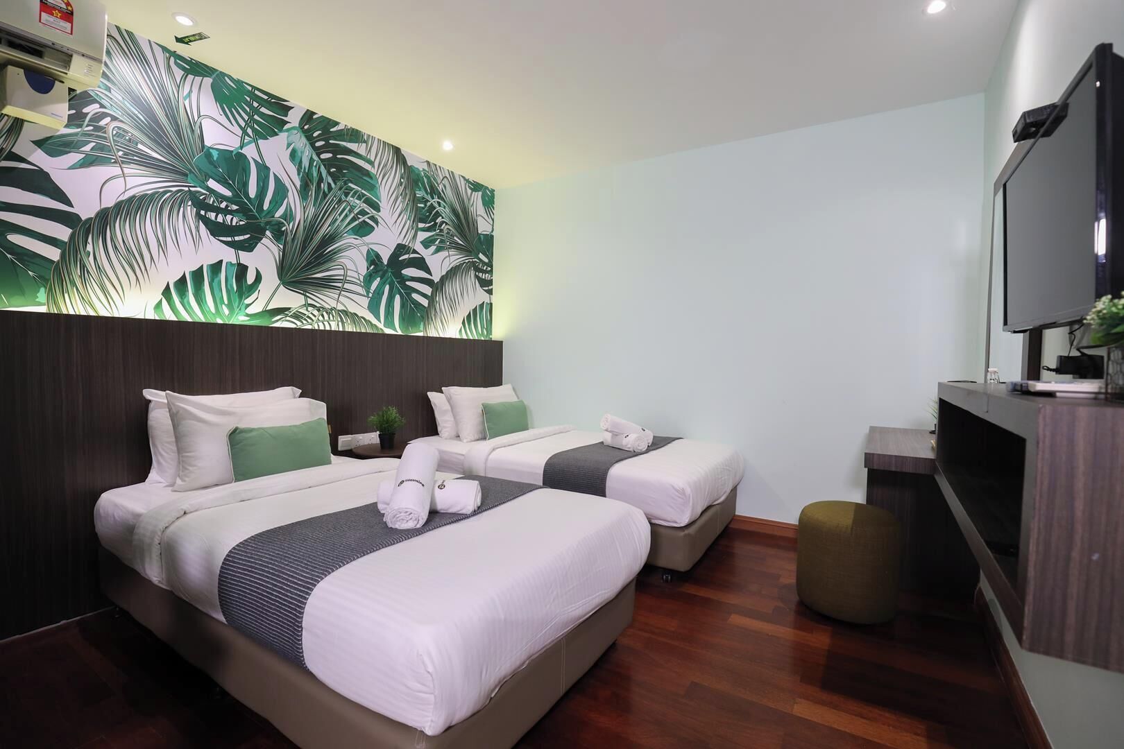 Une chambre d’hôtel avec deux lits, une grande fresque murale, un téléviseur et une petite plante.