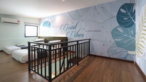 A room with a wooden floor, a black railing, a bed, a desk, and a wall with tropical leaf patterns and the text 'Good Vibes in the tropics'. - Trevor Hotel by I Housing (Malacca City)