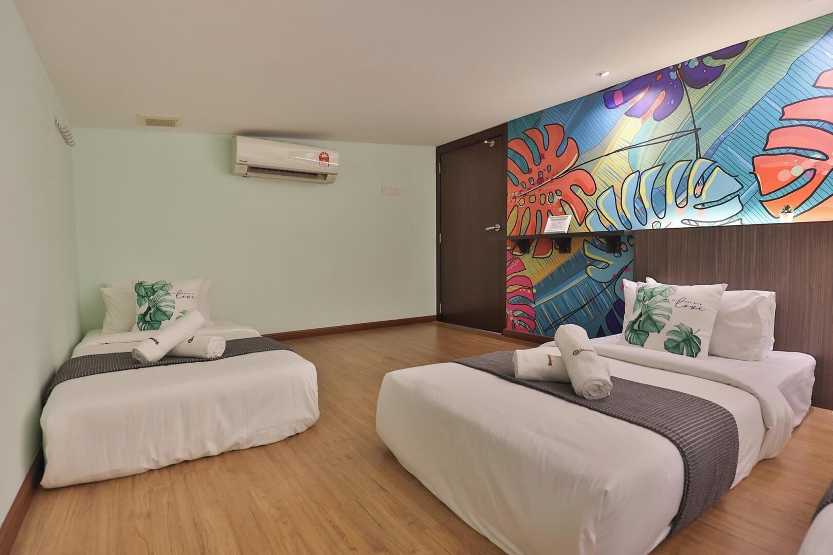 A hotel room with two beds, a colorful mural on the wall, and an air conditioning unit.