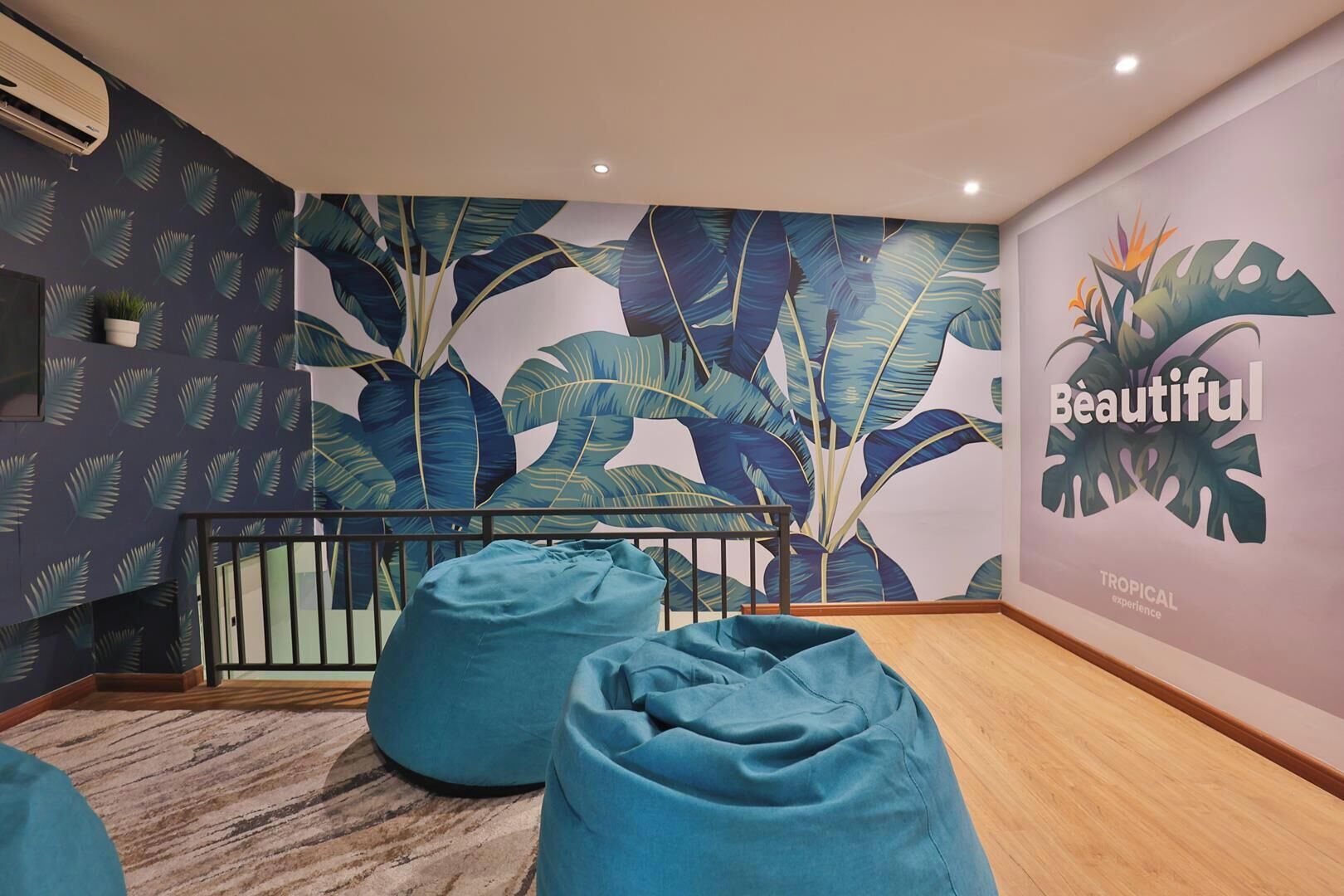 Habitación con papel tapiz de hojas tropicales, suelo de madera y dos pufs.