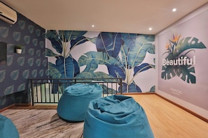 Habitación con papel tapiz de hojas tropicales, suelo de madera y dos pufs.
