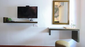 A room with a mounted television, a mirror, and a shelf with a plant and glasses. - Trevor Hotel by I Housing (Malacca City)