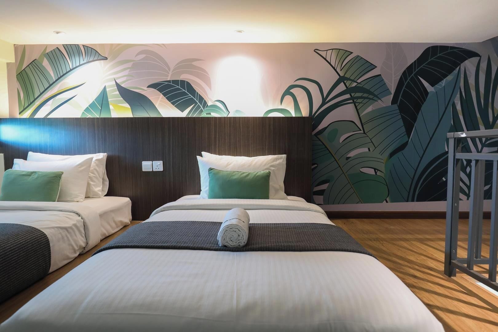 Une chambre d’hôtel avec deux lits, une tête de lit en bois et une grande fresque murale représentant des feuilles tropicales.
