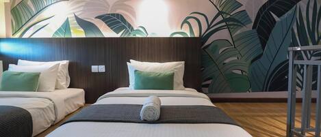 Habitación de hotel con dos camas, cabecera de madera y un mural grande con hojas tropicales en la pared.