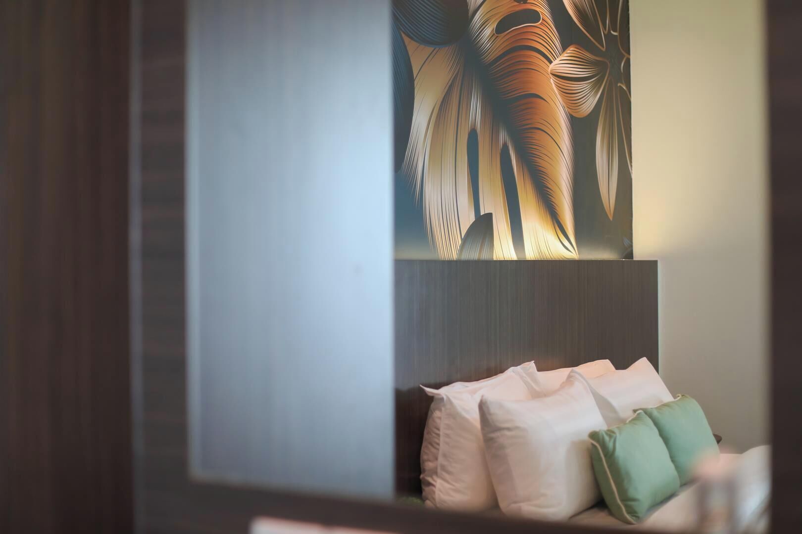 A room with a bed, pillows, and a wall with a leaf pattern.