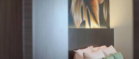 Une chambre avec un lit, des oreillers et un mur orné d’un motif de feuilles.