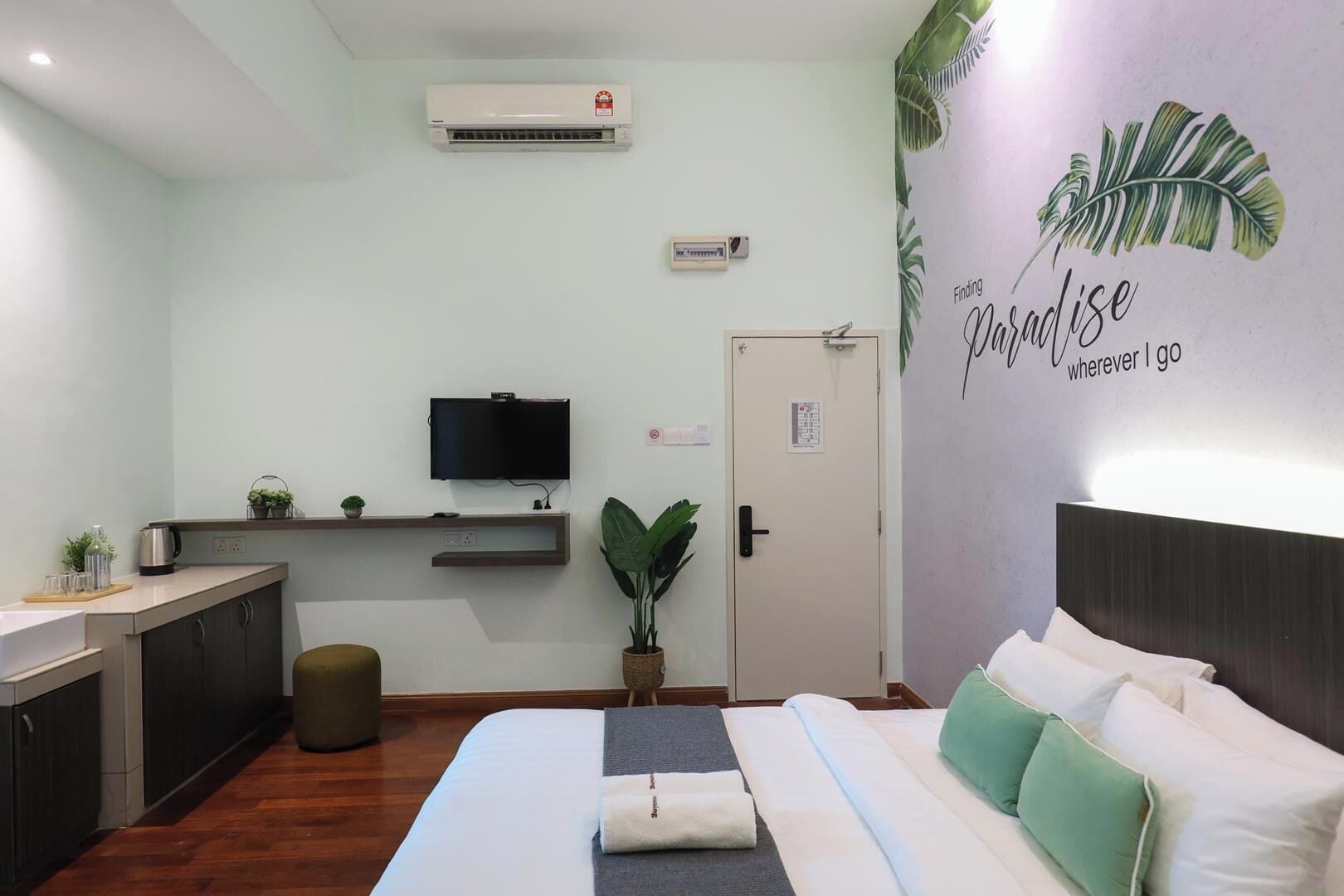 Une chambre d’hôtel équipée d’un lit, d’une télévision, d’une petite kitchenette et d’un mur décoré d’un motif représentant des feuilles.