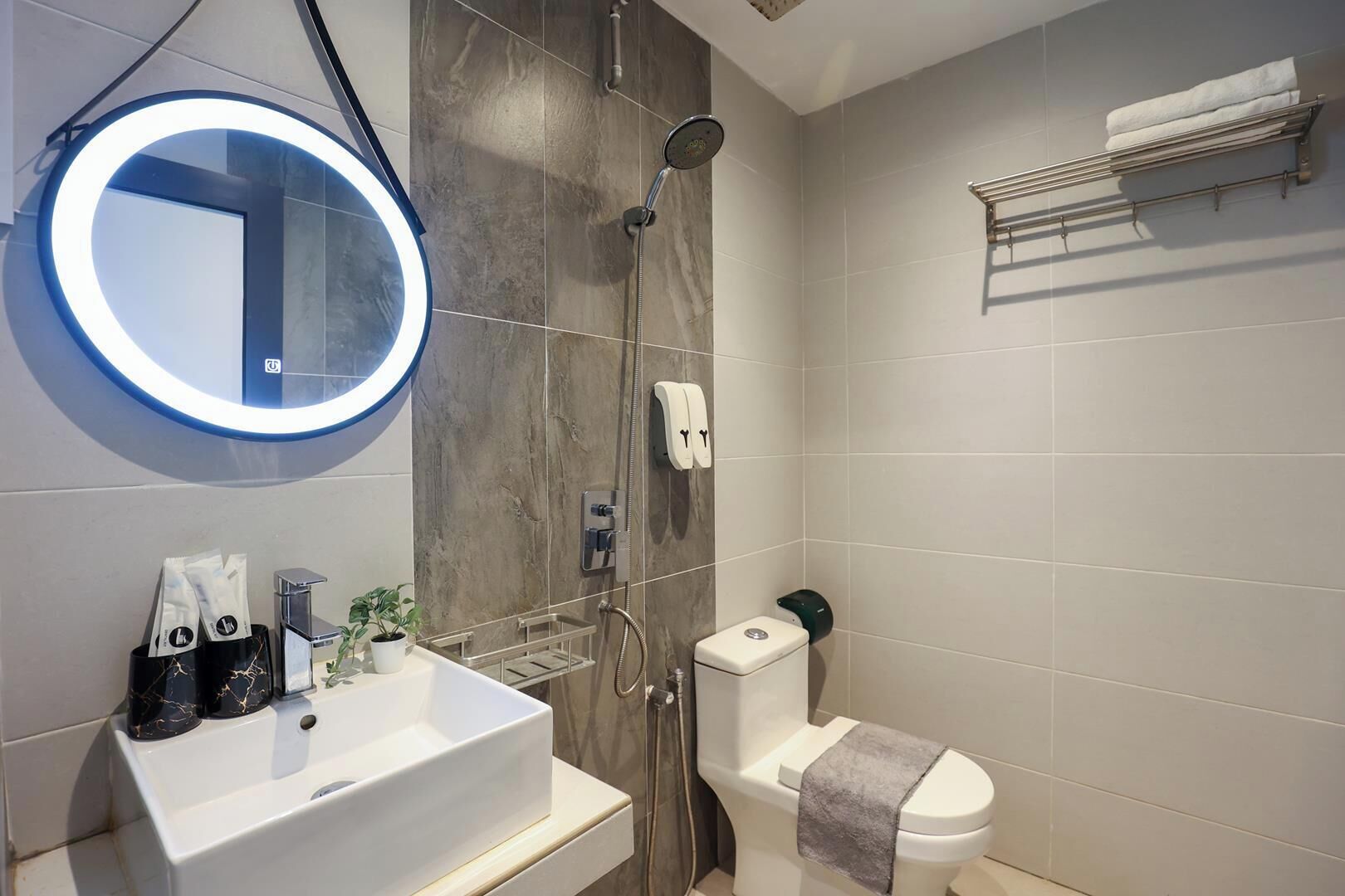 A modern bathroom with a white sink, a round mirror with a blue light, a shower, and a toilet.