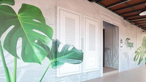 A hallway with a large green plant, white doors, and a wall with a tropical leaf mural. - Trevor Hotel by I Housing (Malacca City)