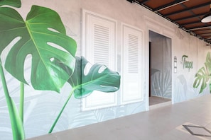 A hallway with a large green plant, white doors, and a wall with a tropical leaf mural. - Trevor Hotel by I Housing (Malacca City)