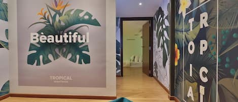 A hallway with a tropical-themed wall mural, a bed, and a wooden floor.